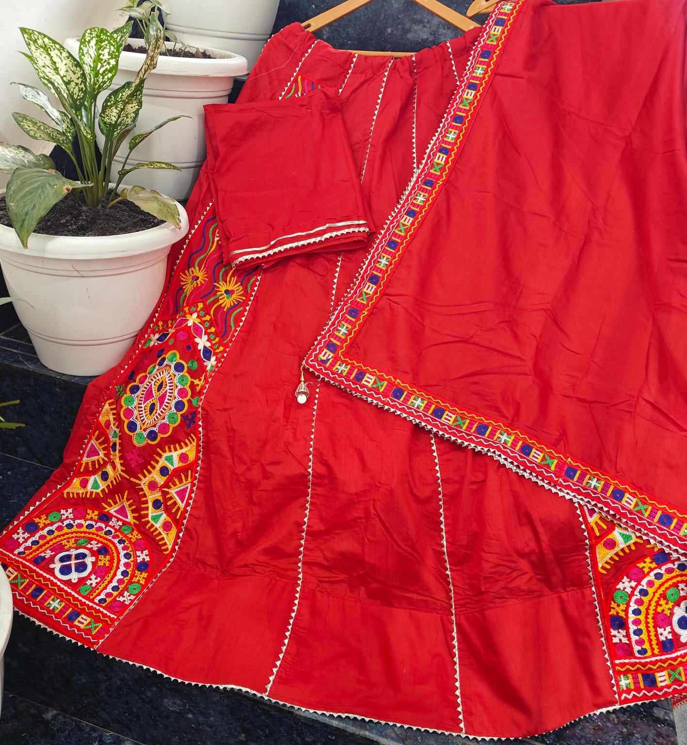 Red traditional outfit with colorful embroidery on a hanger, plant in the background